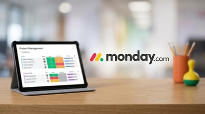 Monday.com logo displayed beside a tablet showing a project management dashboard on a desk.