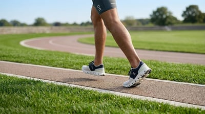 A runner wearing On Running shoes and branded shorts strides along an outdoor athletic track.
