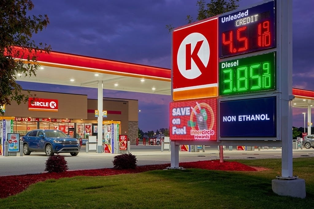 A Circle K gas station and convenience store displays fuel prices on an illuminated roadside sign at dusk.