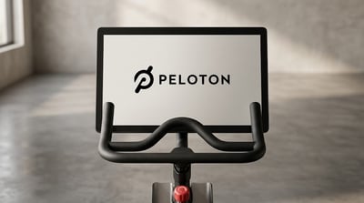 A Peloton stationary exercise bike with the company logo displayed on its touchscreen.