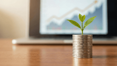 A stack of coins with a small green plant on top sits in front of a laptop displaying an upward-trending stock chart.