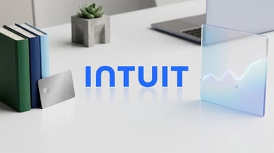 Intuit logo displayed on a white desk beside books, a metal credit card, and a stylized chart panel.