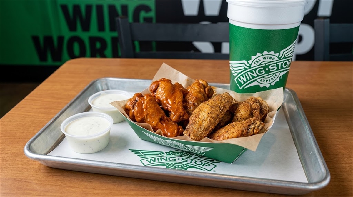 Wingstop-branded tray with chicken wings, dipping sauces, and a cup at a Wingstop restaurant.