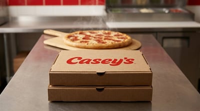 Two Casey's branded pizza boxes sit on a stainless steel counter beside a steaming pepperoni pizza.