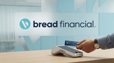 Bread Financial logo on a wall behind a person tapping a Bread Financial credit card on a payment terminal.