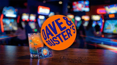 Dave and Buster's logo displayed over a branded game card and cocktail inside an arcade venue.