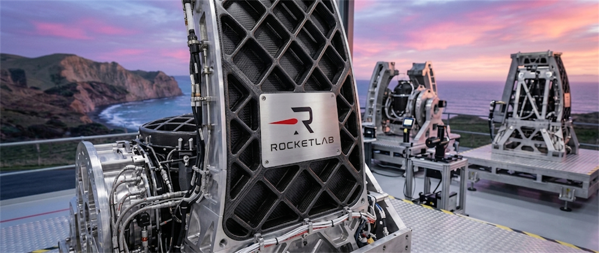 Rocket Lab-branded aerospace hardware on an outdoor platform with a coastal backdrop at sunset.