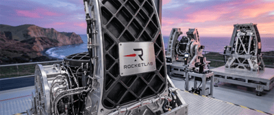 Rocket Lab-branded aerospace hardware on an outdoor platform with a coastal backdrop at sunset.