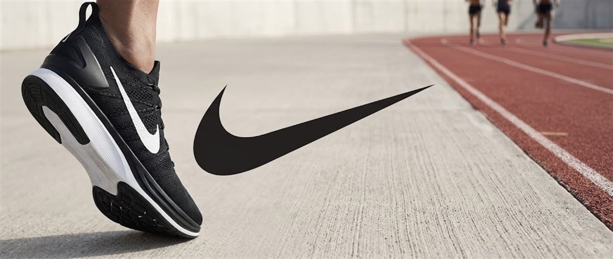 Nike swoosh logo beside a black running shoe on a track with athletes in the background.