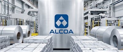 Alcoa logo displayed in an aluminum manufacturing facility with coiled sheets and stacked metal ingots.