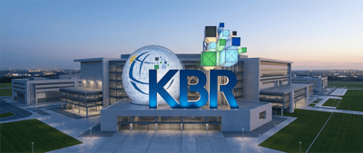 Aerial view of KBR corporate headquarters building with illuminated KBR logo and globe sculpture at dusk.