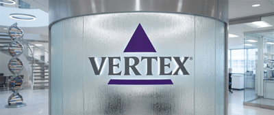 Vertex Pharmaceuticals logo displayed on a glass wall in an office lobby with a DNA helix sculpture nearby.