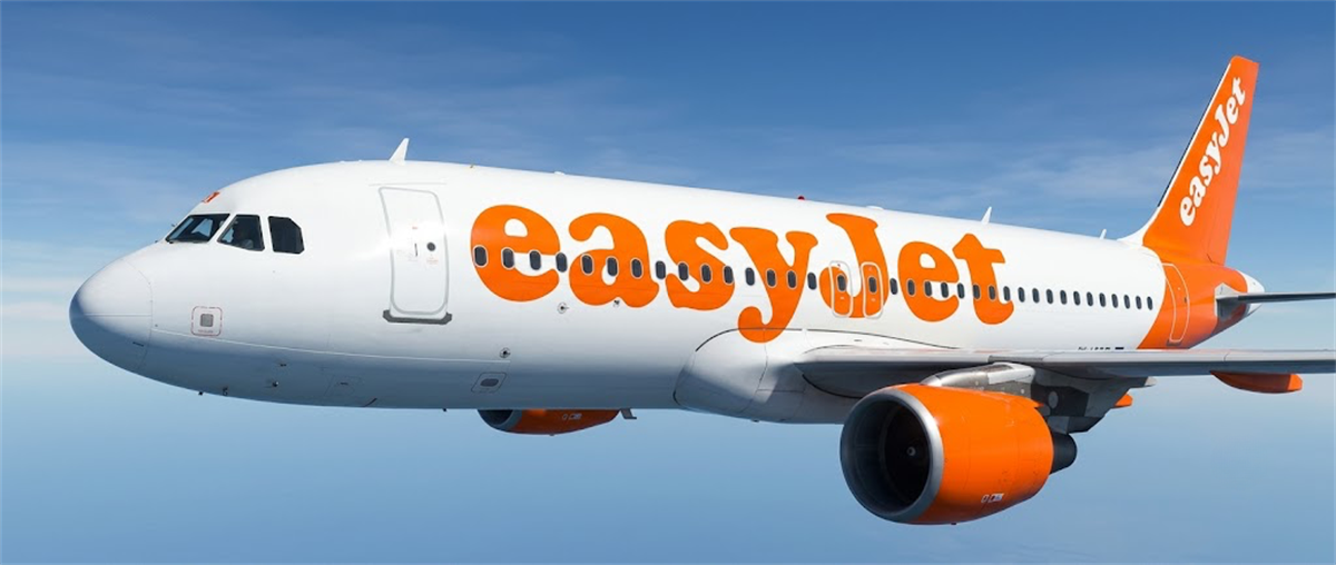 An easyJet passenger jet with orange livery and logo flying above clouds against a blue sky.