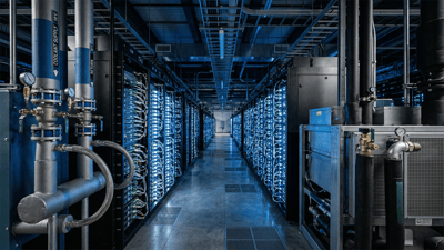 Data center aisle with server racks, blue lighting, and coolant supply and return pipes with gauges.