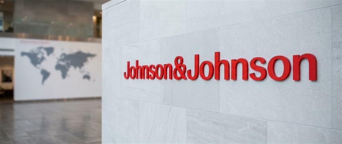 Johnson & Johnson logo displayed in red lettering on a stone wall in a corporate lobby with a world map backdrop.
