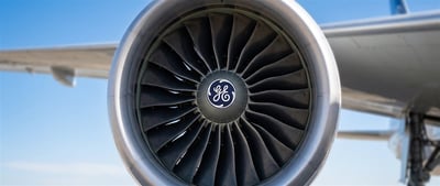 Close-up of a GE jet engine turbine with the General Electric logo mounted on an aircraft wing.