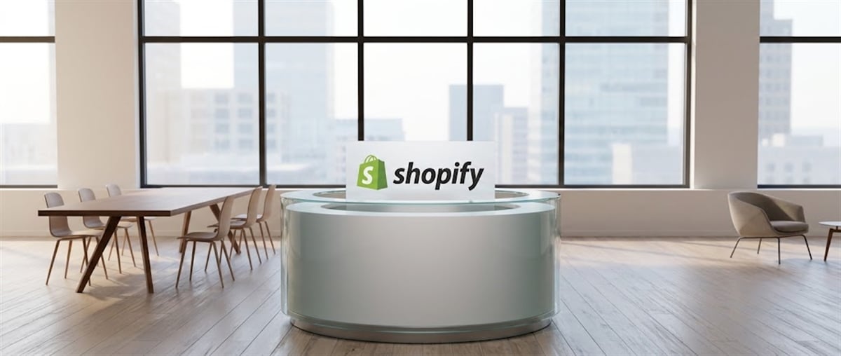 Shopify logo displayed on a sign at a round reception desk in a modern office with city views.