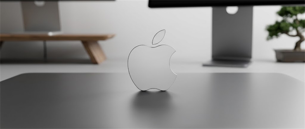 A translucent Apple logo stands on a desk in front of monitors and a small bonsai tree.