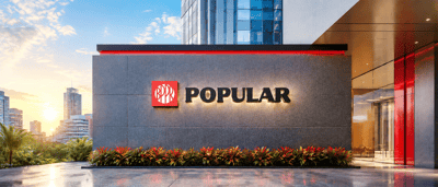Popular Inc. logo displayed on the exterior wall of a modern corporate building at sunset.