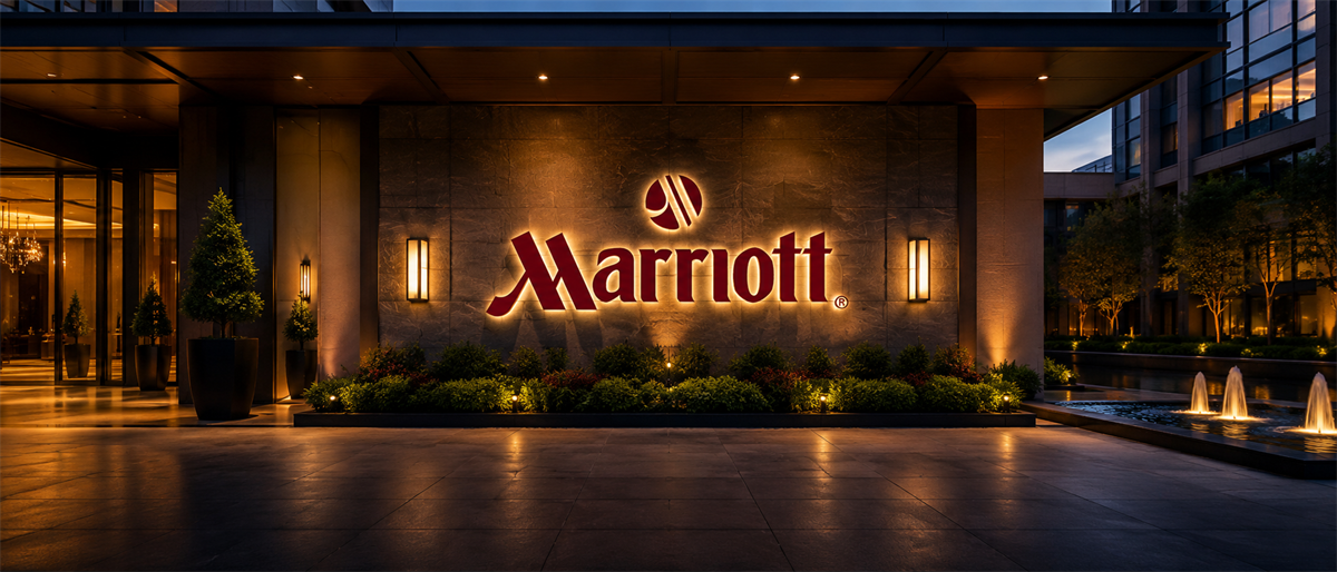 Illuminated Marriott logo and sign at the entrance of a hotel building at dusk.