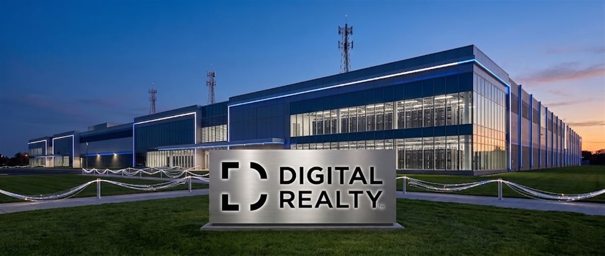 Digital Realty data center building with illuminated exterior and a ground-level sign displaying the company logo at dusk.