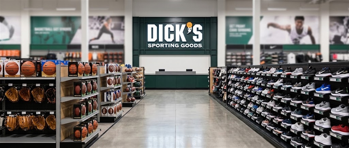 Interior of a Dick's Sporting Goods store showing shelves of basketballs, gloves, and a wall of shoes.