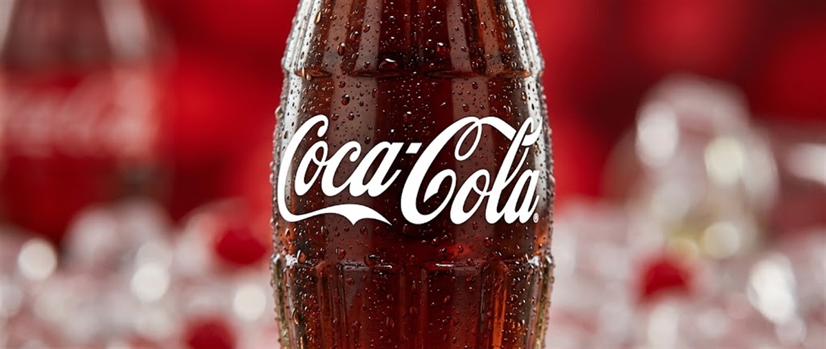 Condensation-covered glass Coca-Cola bottle with the company logo, set against a blurred red background.