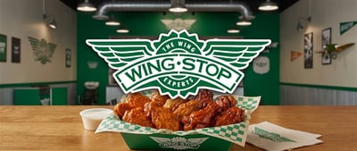 Wingstop logo displayed over a basket of chicken wings inside a restaurant dining area.