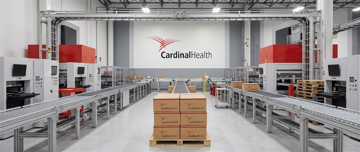 Cardinal Health branded boxes on pallets sit amid automated conveyor systems in a distribution warehouse.