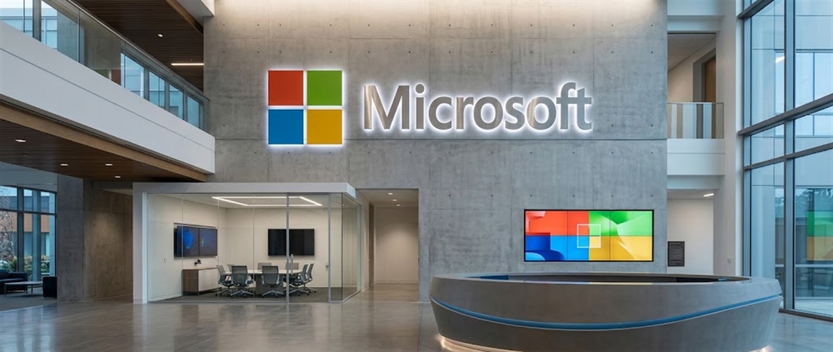 Microsoft logo and sign displayed in the lobby of a corporate office building with a glass meeting room.