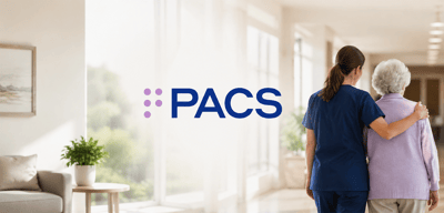 PACS Group logo beside a caregiver walking arm in arm with an elderly woman in a care facility hallway.