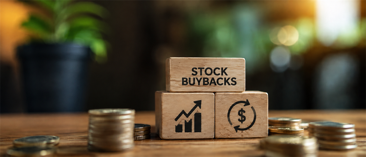 Wooden blocks reading "Stock Buybacks" with chart and dollar icons, surrounded by stacked coins on a table.