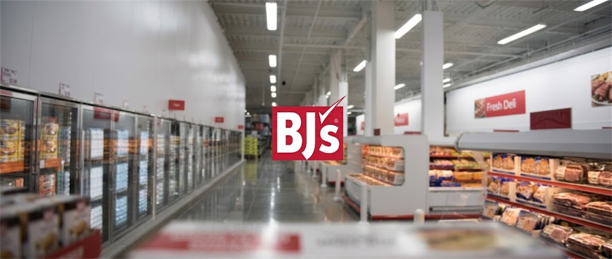 BJ's Wholesale Club logo overlaid on a store interior showing refrigerated aisles and a fresh deli section.