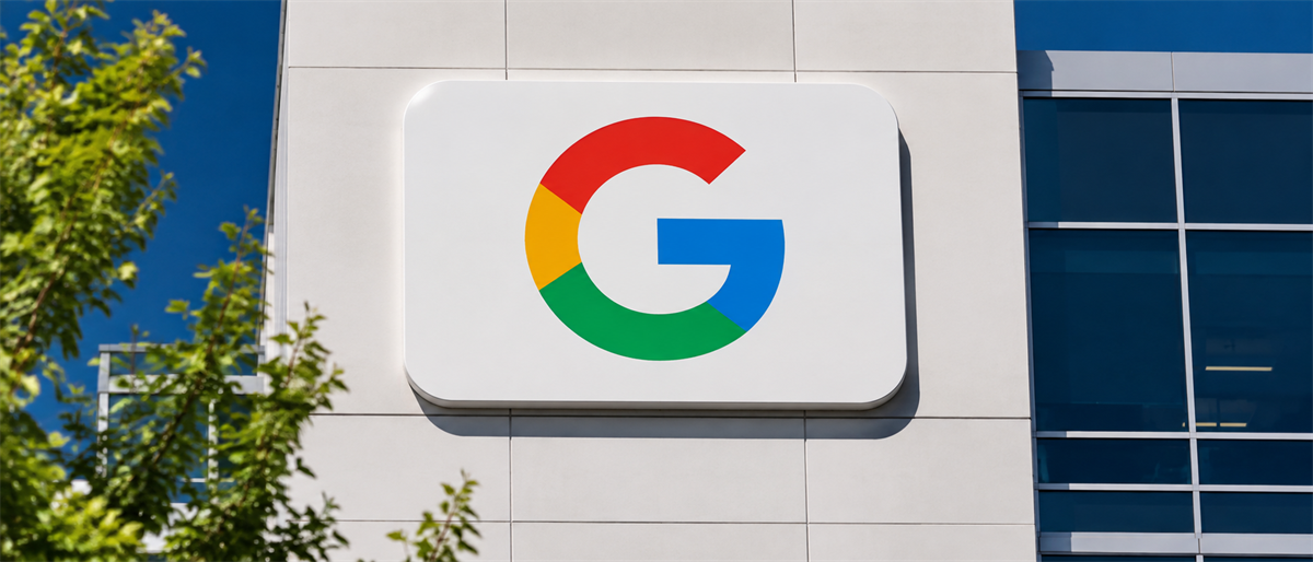 Google logo sign mounted on the exterior wall of an office building with trees in foreground.