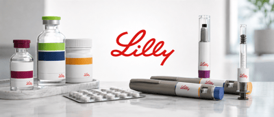 Eli Lilly logo displayed among medicine vials, pill bottles, blister packs, and injector pens on a table.