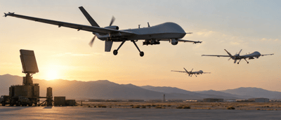 Three military surveillance drones fly near a mobile radar unit at an airfield during sunset.