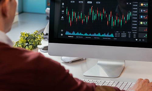 Person viewing a desktop monitor displaying multiple candlestick charts and market data, representing ETF screening and portfolio analysis.