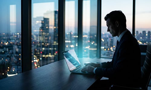 Business professional working on a laptop in a high-rise office at dusk, overlooking a city skyline, suggesting insider trading activity or executive-level market monitoring.