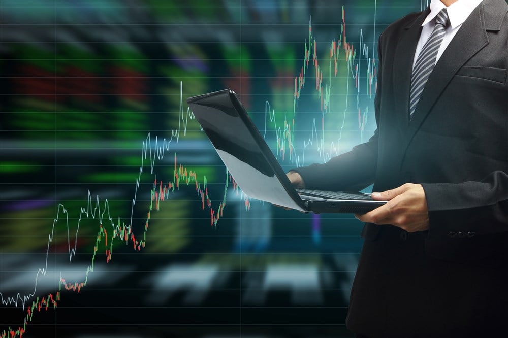 Business man typing on laptop with technical background displaying stock charts