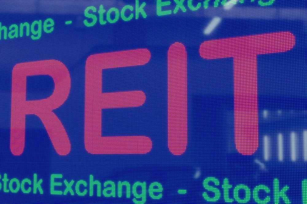REITs (Real Estate Investment Trusts) on a blue LED screen framed by the text stock exchange in green. Real estate concept, 3D illustration.