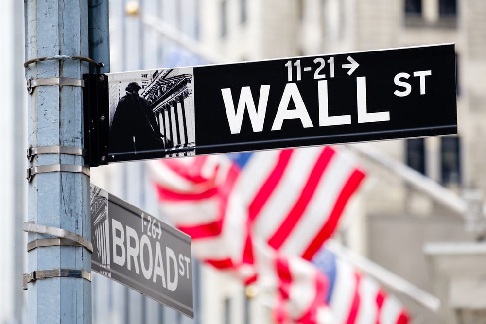 Wall street sign in New York City with out of focus buildings and american flags on the background