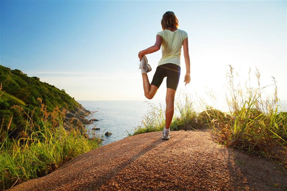 woman stretching on top of hill at sunset