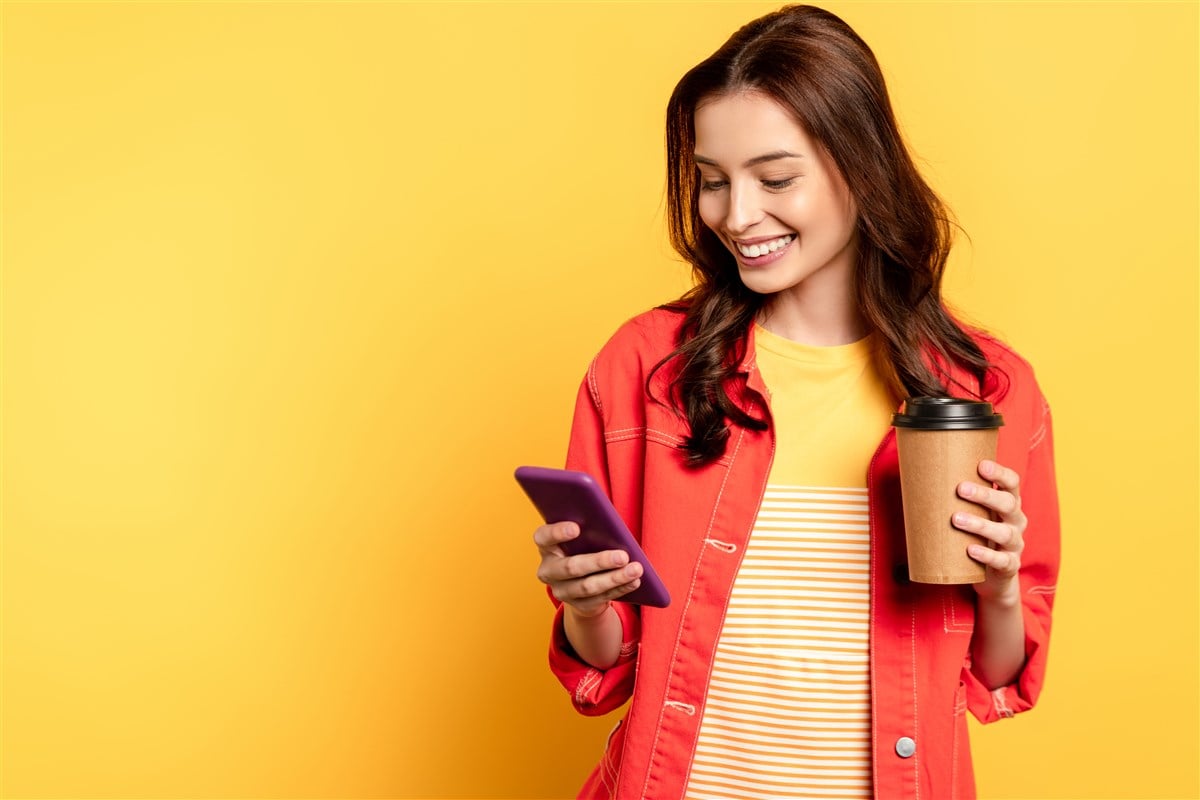 woman holding mobile phone in one hand and cup in another