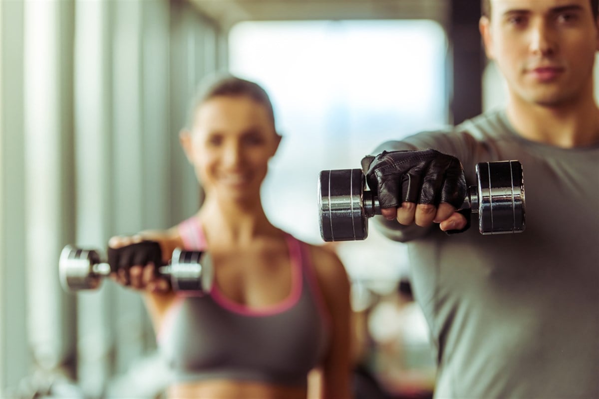 Attractive young muscular people working out with dumbbells in gym; Celsius stock 