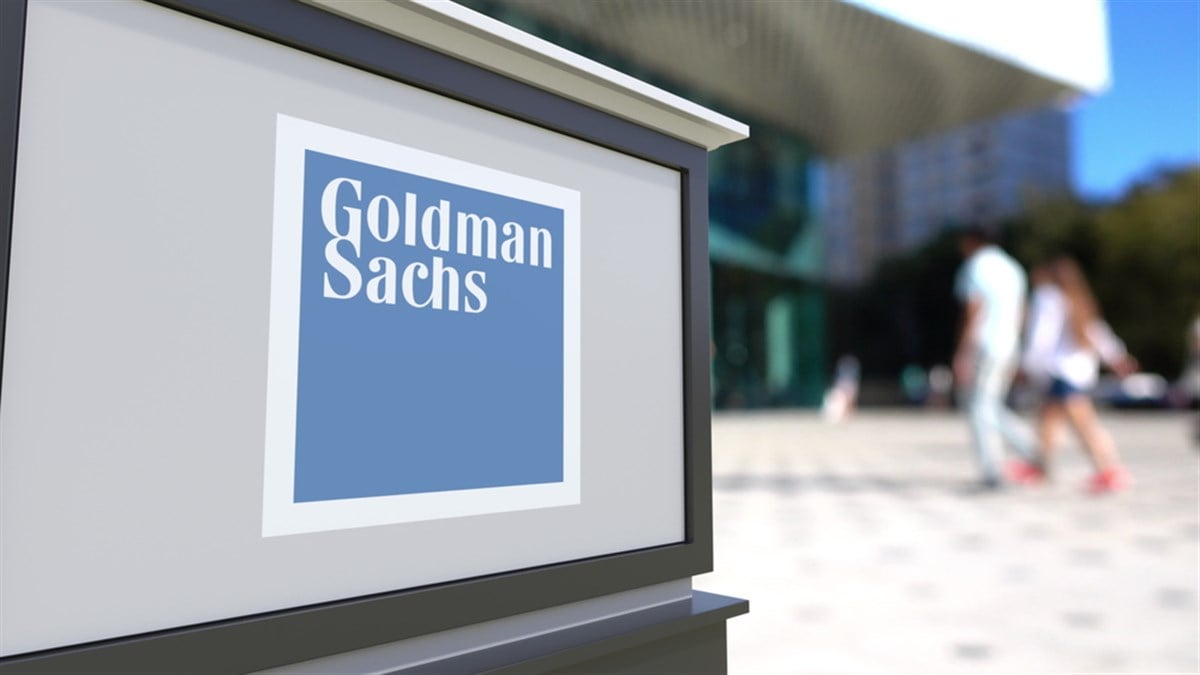 Street signage board with The Goldman Sachs Group Inc. logo. Blurred office center and walking people background. 