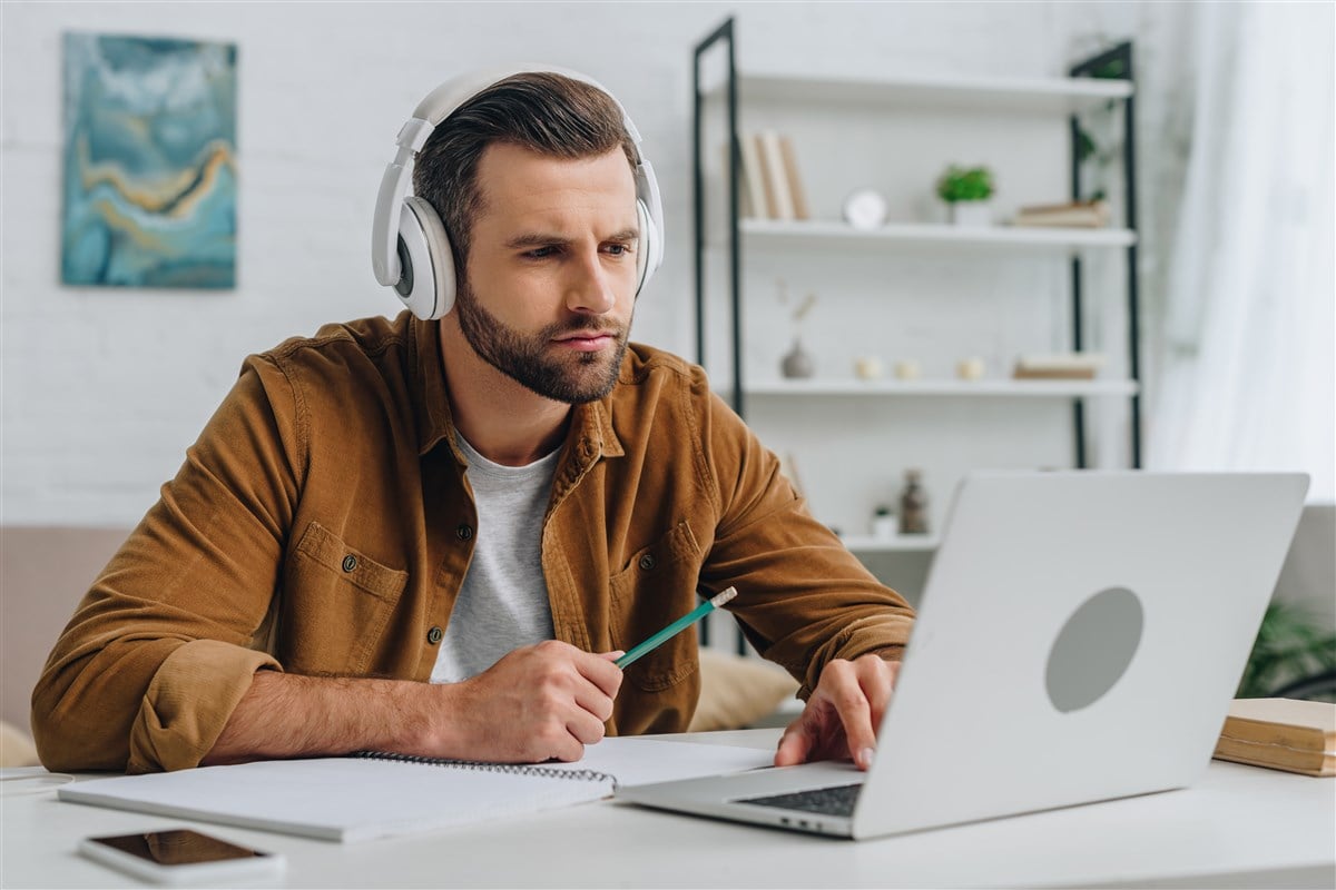 photo of man sitting in front of laptop with headphones on taking online course