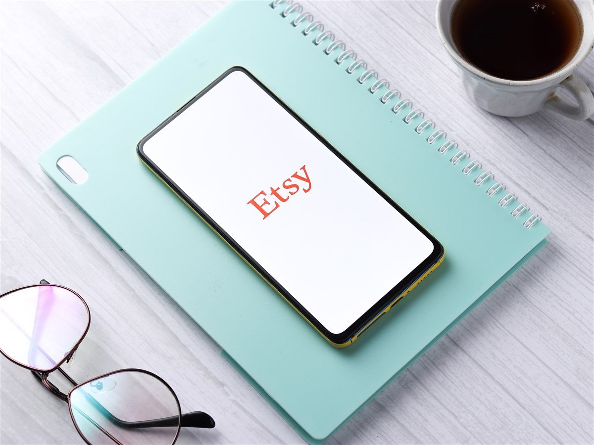 photo of mobile device with Etsy logo displayed laying on planner with glasses and coffee in background