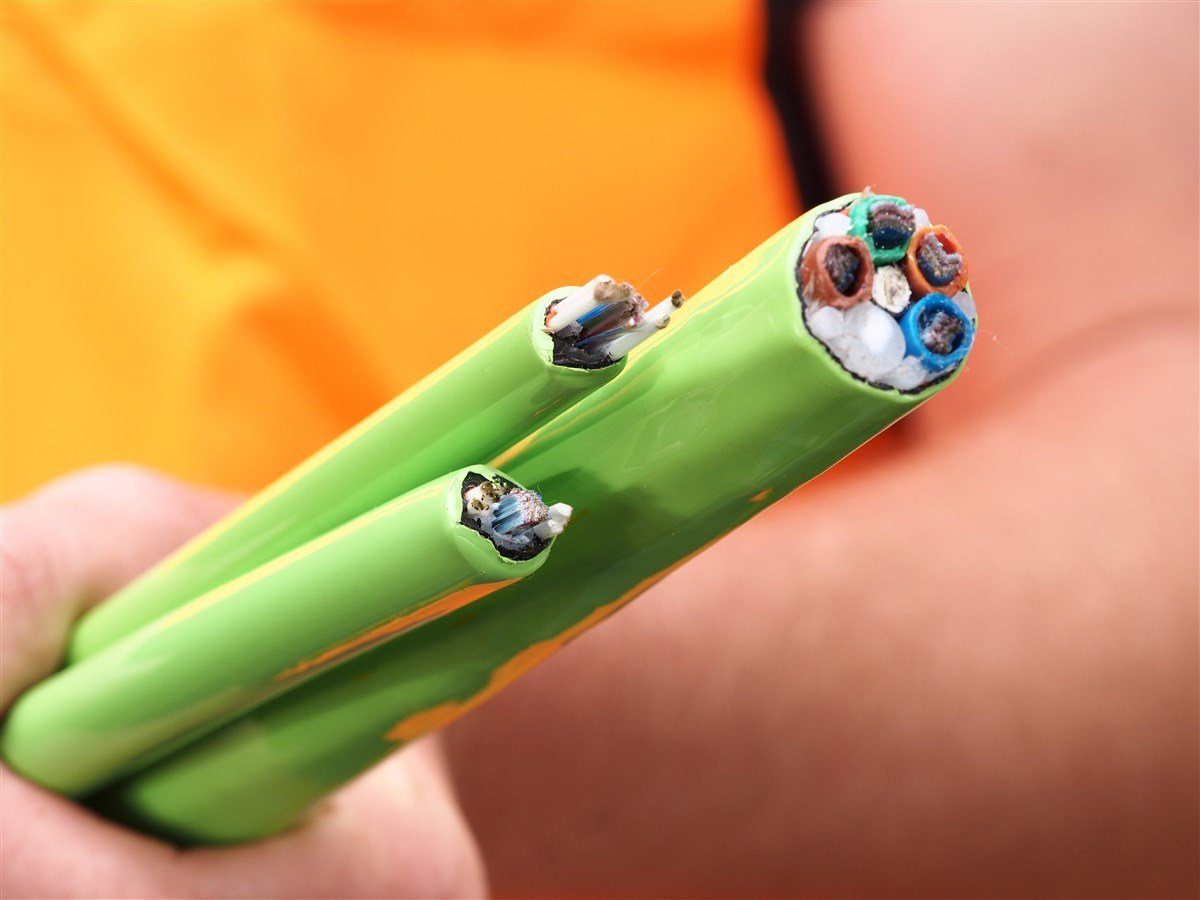 close-up of green fiber optic cable with part of hand in background  