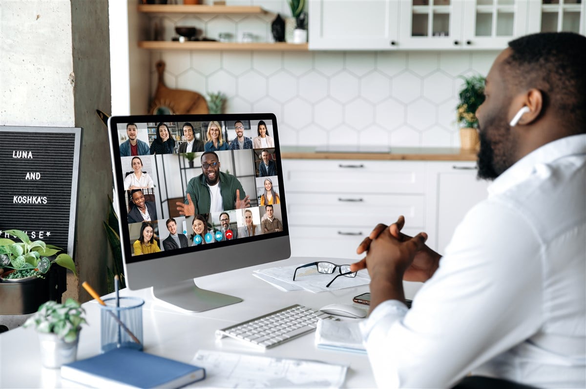 man on zoom call with computer screen showing other teleconference attendees