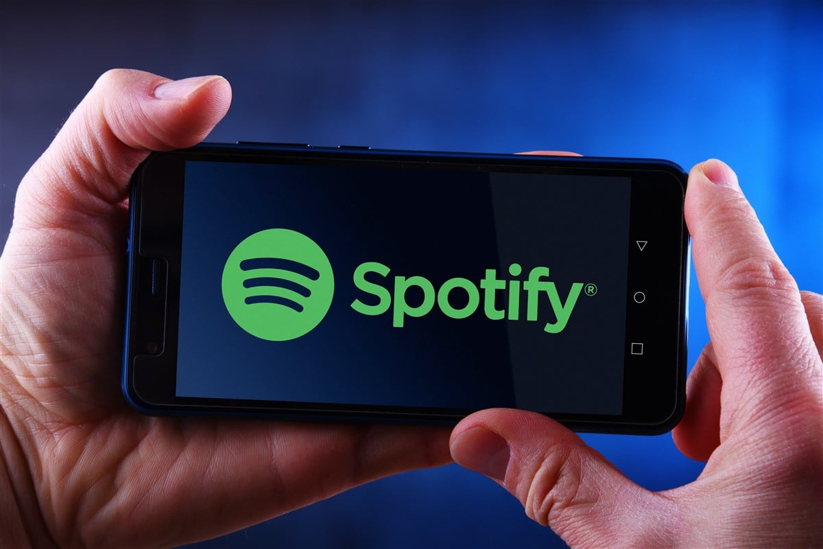 Picture of man's hands holding smartphone with Spotify logo displayed